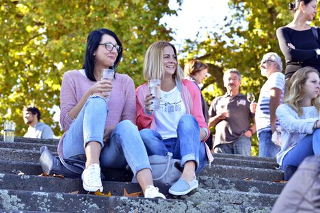 Zwei junge Frauen mit Weingläsern auf Stufen am Rheinufer